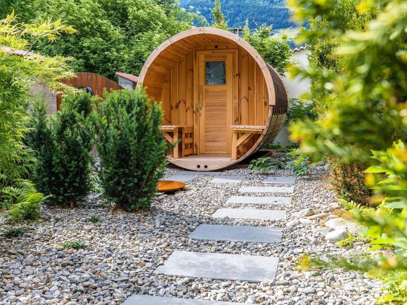 Runder Holz-Gartenpavillon mit kleinem Fenster, umgeben von Kies und grünen Pflanzen.