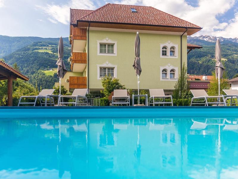 Hellgrünes Haus mit rotem Dach, Swimmingpool im Vordergrund, Berglandschaft im Hintergrund.