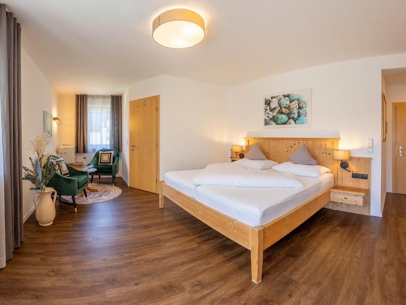 Helles, modernes Schlafzimmer mit Holzbett, großen Fenstern, Pflanzen und warmem Holzfußboden.