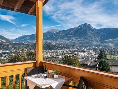Balkon mit Tisch und Stühlen mit Blick auf Berge und ein Tal unter blauem Himmel.