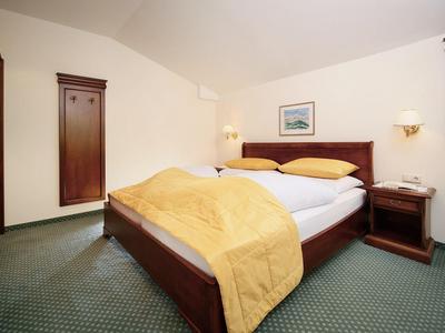 Schlichtes Schlafzimmer mit Holzbett, gelber Bettdecke, Nachttisch und grünem Teppichboden.