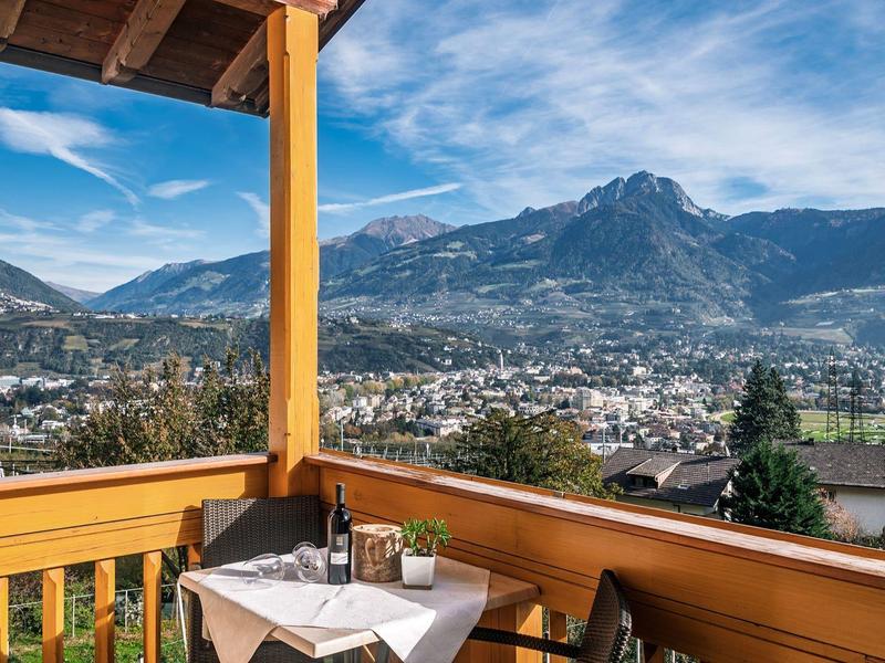 Balkon mit Tisch, Stühlen und Bergblick unter blauem Himmel mit vereinzelten Wolken.