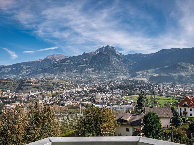 Stadt mit Häusern vor grünen Hügeln und Bergen unter blauem Himmel mit Wolken.