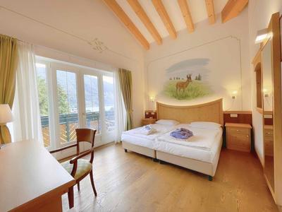 Helles Hotelzimmer mit Doppelbett, Holzbalkendecke und Balkon mit Blick ins Grüne.