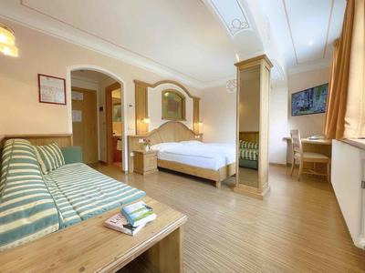 Geräumiges Schlafzimmer mit Holzboden, Doppelbett, gestreiftem Sofa und großem Fenster mit Vorhängen.