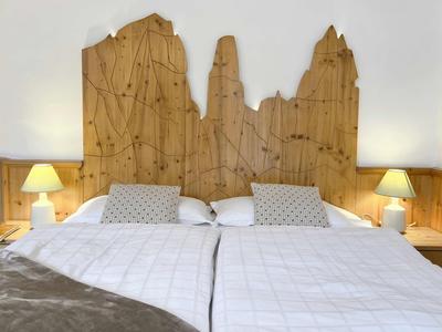 Zwei Einzelbetten mit weißer Bettwäsche, Holz-Vertäfelung und "Baum"-förmigem Kopfteil, je mit Lampe.