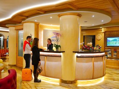 Helle Hotellobby mit rundem Empfangstresen, Holzvertäfelung und zwei Gästen mit Gepäck.