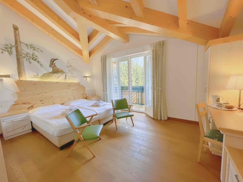 Hell eingerichtetes Schlafzimmer mit Holzbalken, zwei Betten, grünen Stühlen und großer Fensterfront.