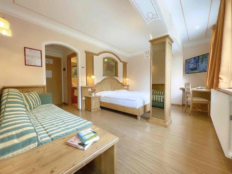 Geräumiges Schlafzimmer mit Holzboden, Doppelbett, gestreiftem Sofa und großem Fenster mit Vorhängen.