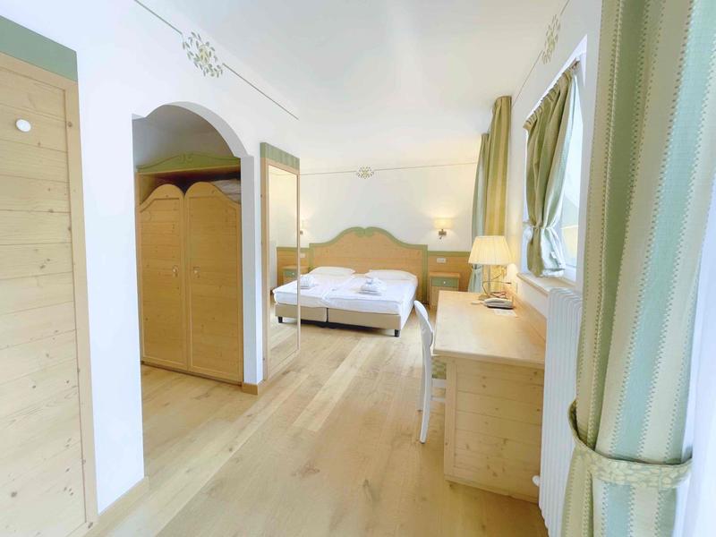 Helles Schlafzimmer mit Holzboden, Doppelbett, Gardinen und Holzmöbeln in natürlichen Farben.