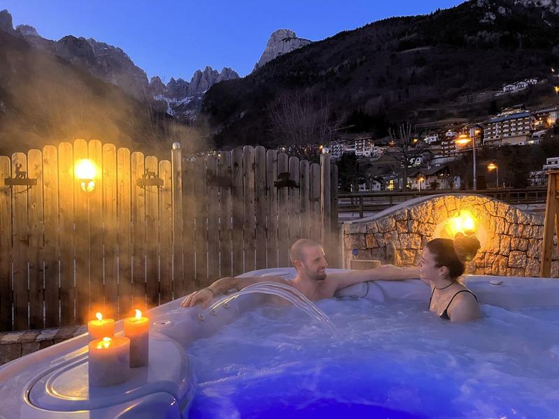 Zwei Menschen entspannen im Whirlpool bei Kerzenlicht und Bergkulisse in der Dämmerung.