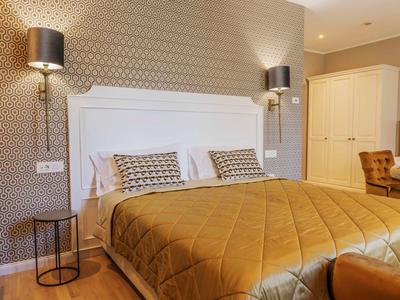 Chambre d'hôtel moderne avec grand lit, couvre-lit doré et lampes murales élégantes.