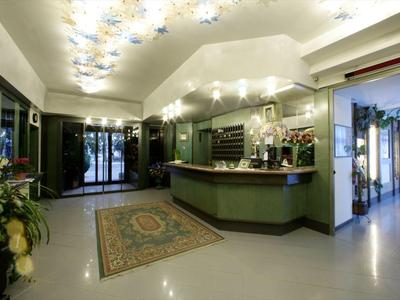 Réception d'hôtel lumineuse avec comptoir vert, tapis et arrangements floraux.