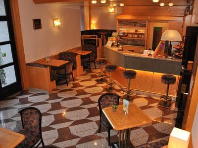 Espace café chaleureux avec plusieurs tables, chaises et un comptoir de bar aux tons chauds.