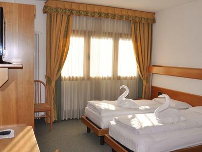 Chambre d'hôtel avec deux lits simples, bureau, chaise et fenêtres avec rideaux dorés.