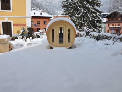 Pod d'hôtel rond jaune dans la neige avec bâtiments et sapin derrière.