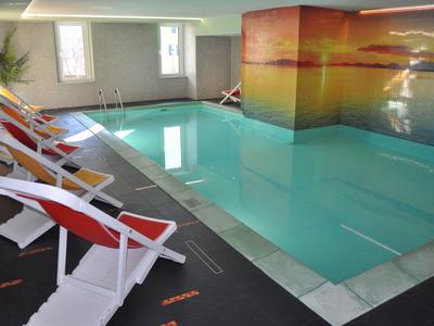 Innenpool mit weißen Liegestühlen und Wandbild eines Sonnenuntergangs