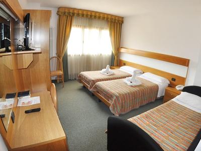 Chambre d'hôtel avec deux lits simples, bureau, télévision et fenêtre avec rideaux.