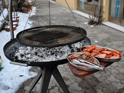Grill avec grille et assiettes de saucisses à côté d'un chemin enneigé.