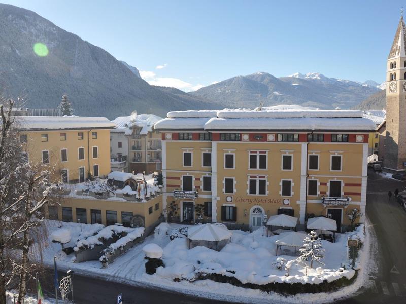 Bâtiment d'hôtel avec cour enneigée et montagnes en arrière-plan sous un ciel clair.