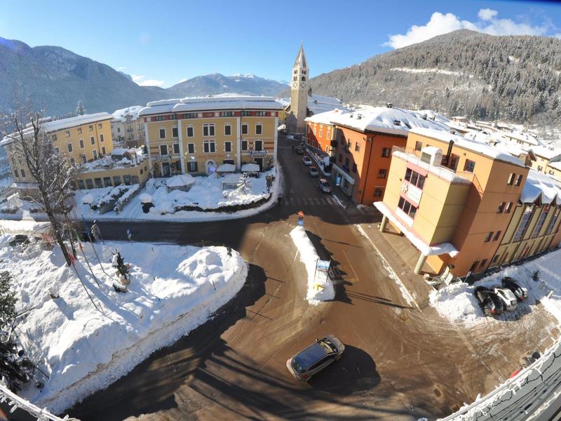 Vue sur un village enneigé avec un paysage montagneux et plusieurs bâtiments sous un ciel clair.