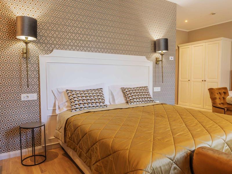 Chambre d'hôtel moderne avec grand lit, couvre-lit doré et lampes murales élégantes.