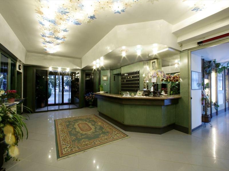 Réception d'hôtel lumineuse avec comptoir vert, tapis et arrangements floraux.