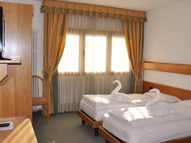 Chambre d'hôtel avec deux lits simples, bureau, chaise et fenêtres avec rideaux dorés.