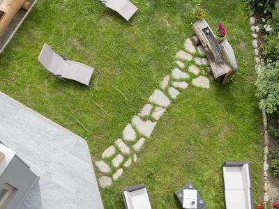 Groene tuin met ligstoelen, terras en geplaveid pad.