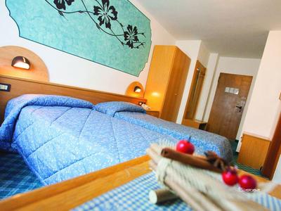 Hotelkamer met twee bedden en blauwe beddengoed, tafel met decoratie en gangdeur op de achtergrond