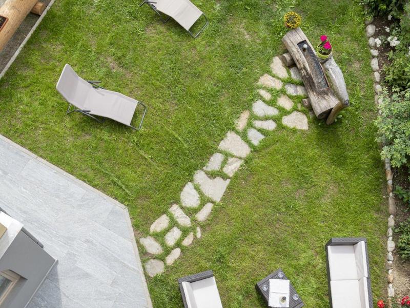 Groene tuin met ligstoelen, terras en geplaveid pad.