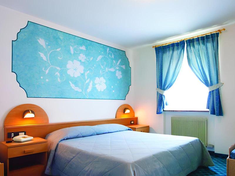 Een lichte hotelkamer met blauwe wanddecoratie, tweepersoonsbed en blauwe gordijnen.