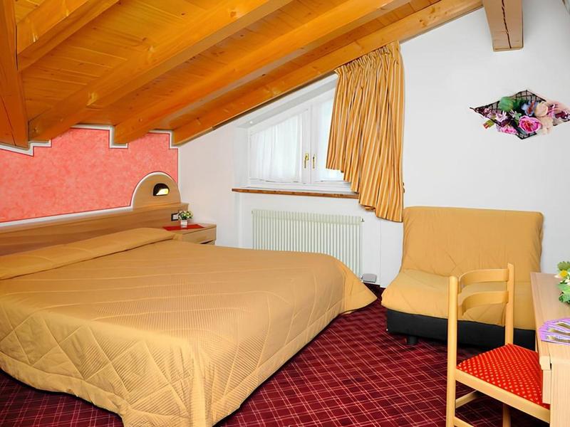 Gezellige hotelkamer met schuine plafond, tweepersoonsbed en fauteuil in warme tinten.