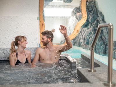 Couple se détend dans un jacuzzi avec vue sur la piscine et un mur rocheux.