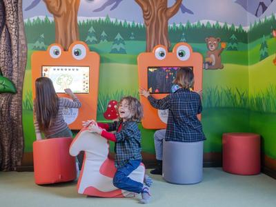 Des enfants jouent de manière interactive sur des panneaux de jeu orange dans une pièce colorée avec des motifs de forêt