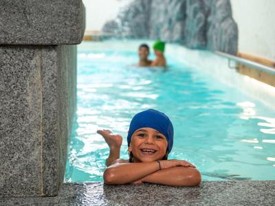 Enfant heureux avec bonnet de bain se repose au bord d'une piscine intérieure