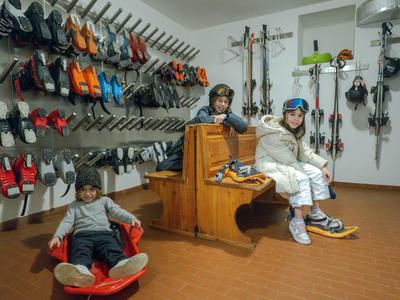 Trois personnes dans un magasin de location de ski entourées de skis et snowboards au mur.