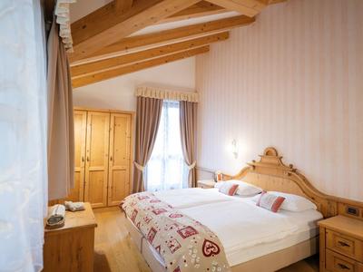 Chambre confortable avec poutres en bois, lit double et grands rideaux sur deux fenêtres.