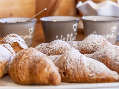 Plusieurs croissants sur une planche en bois avec trois tasses grises en arrière-plan