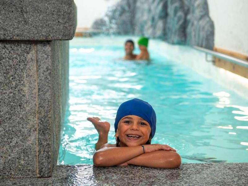Enfant heureux avec bonnet de bain se repose au bord d'une piscine intérieure