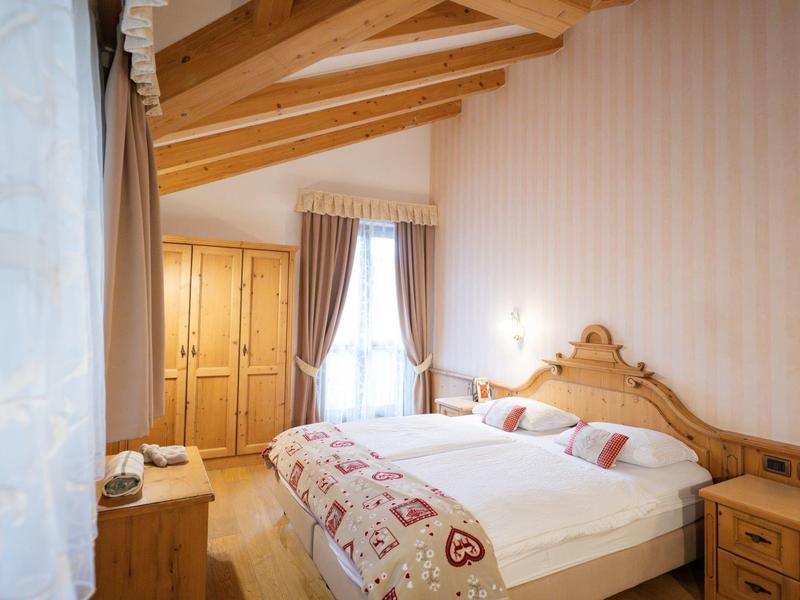 Chambre confortable avec poutres en bois, lit double et grands rideaux sur deux fenêtres.