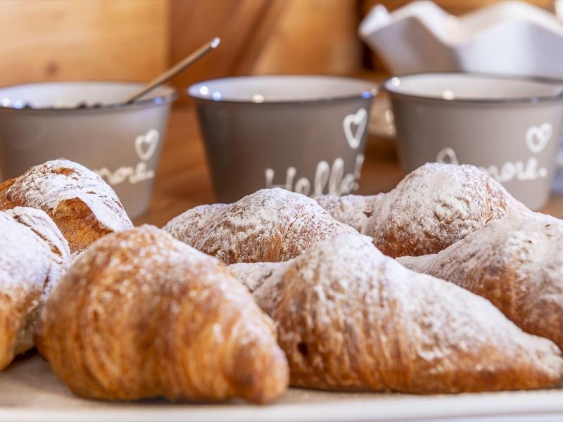 Plusieurs croissants sur une planche en bois avec trois tasses grises en arrière-plan