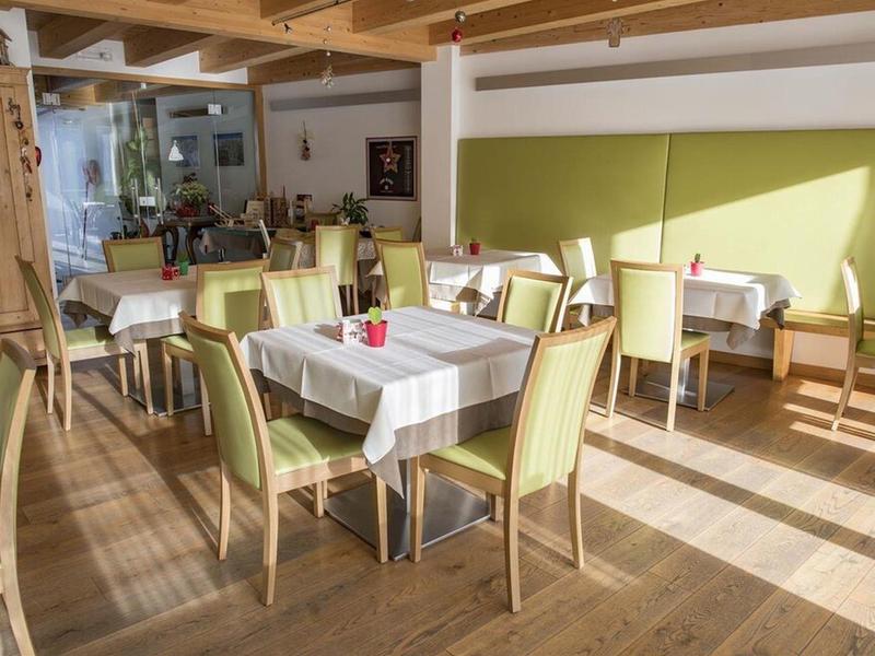 Sala da pranzo luminosa con più tavoli e sedie verdi alla luce naturale.