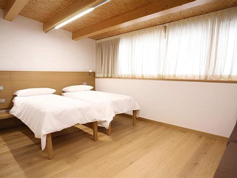Camera d'albergo luminosa con due letti singoli, pavimento in legno e travi a vista.
