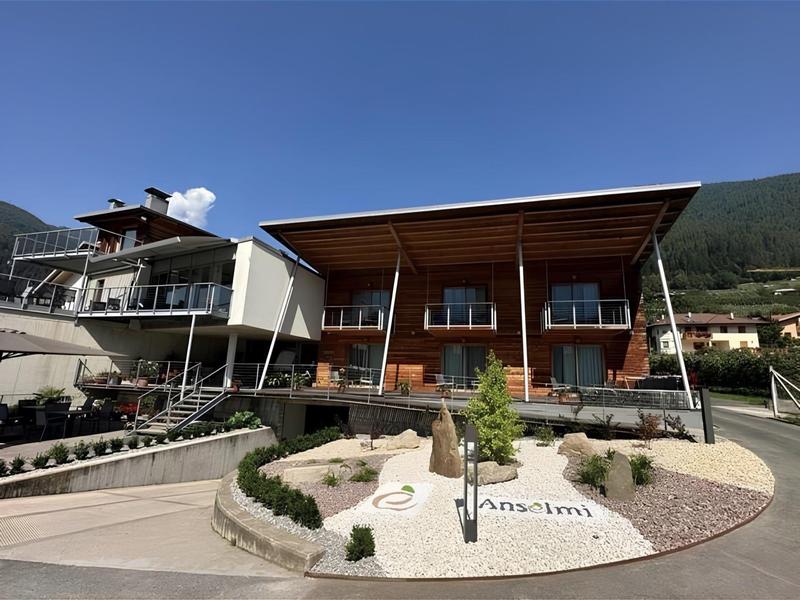 Edificio moderno di un hotel con facciata in legno e sfondo montano sotto un cielo sereno.