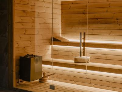 Moderní dřevěná sauna se skleněnou stěnou, dřevěnými lavicemi a nepřímým osvětlením.