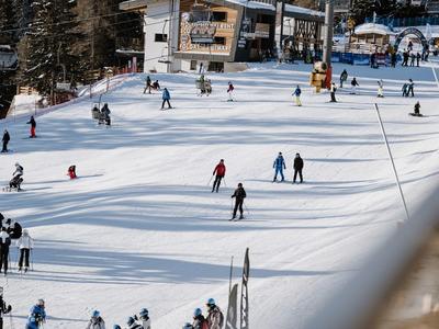 Několik lidí lyžuje na zasněženém svahu před skihotelem v horském středisku.