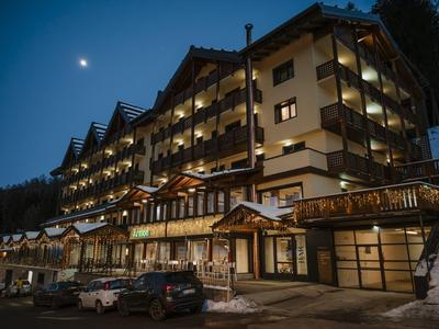 Grande edificio dell'hotel con balconi illuminati di notte e terreno coperto di neve.