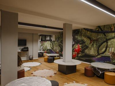 Pohodlná hotelová lounge s kulatými stoly, stoličkami a nástěnnou malbou s přírodním motivem