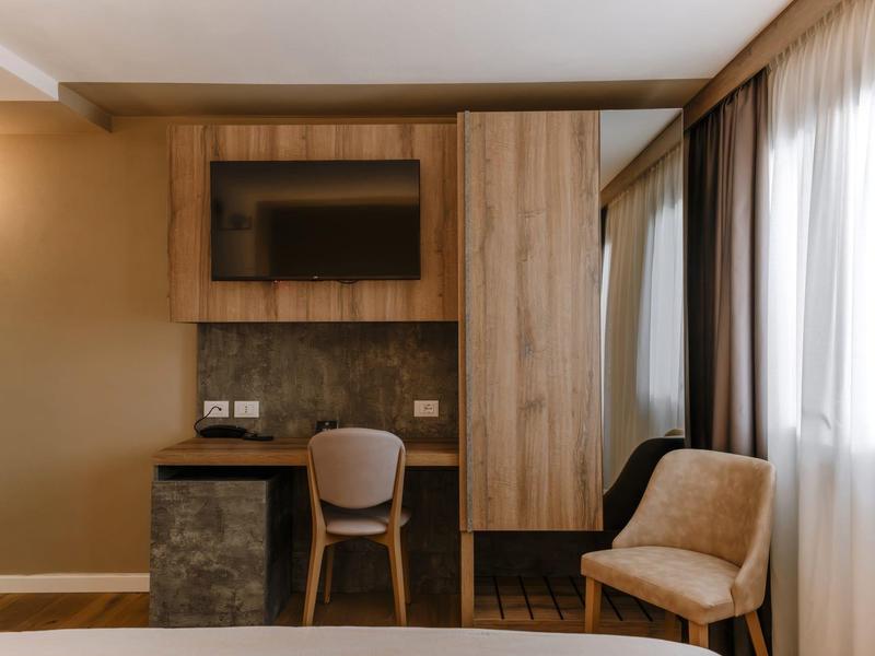 Moderní pracovní prostor v hotelovém pokoji se židlí, televizí a skříní vedle okna se závěsy.